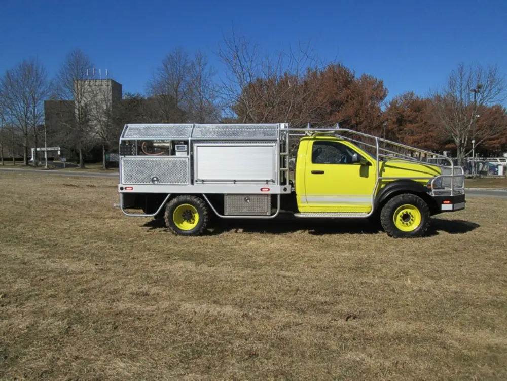 Exterior view of small fire truck showing cab, body compartments, and wheel/tire area.