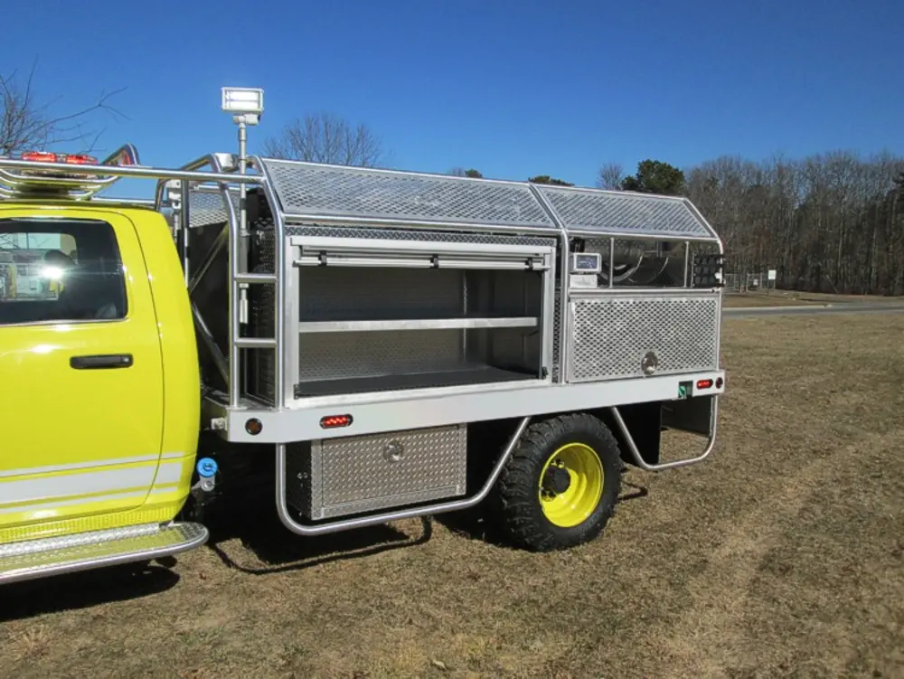 Exterior view of small fire truck showing cab, body compartments, and wheel/tire area.