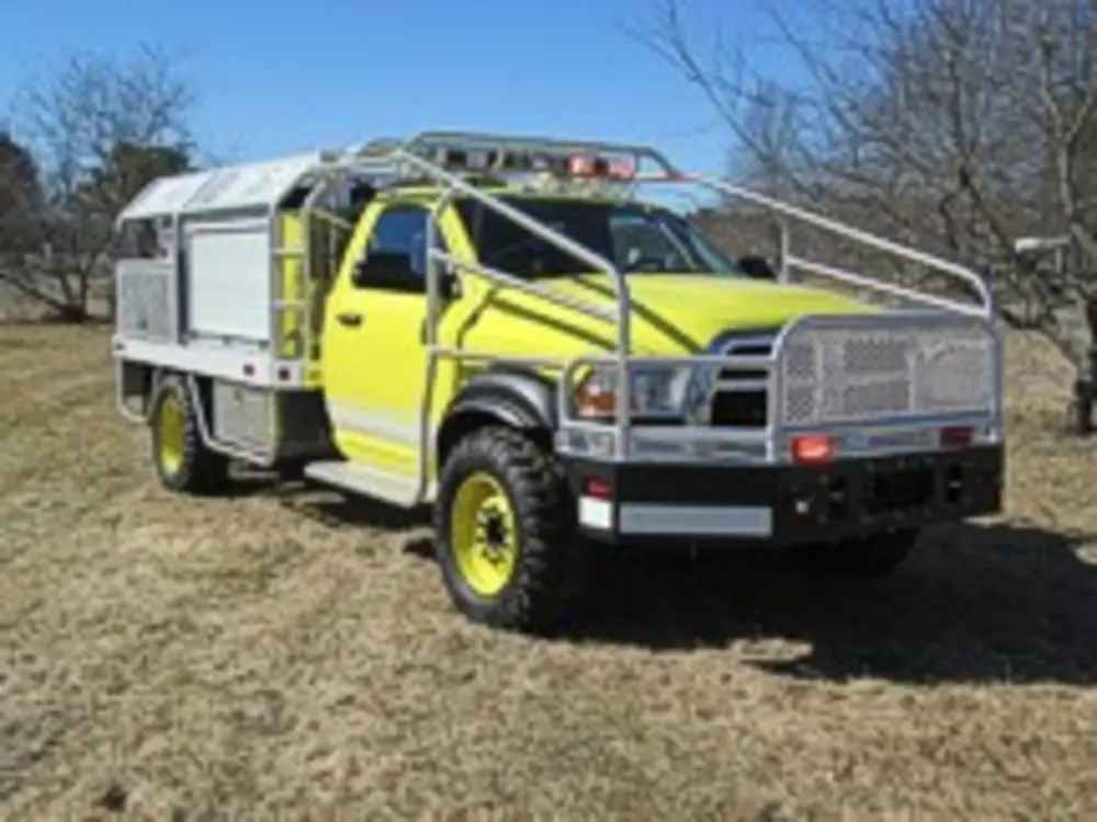 Exterior view of small fire truck showing cab, body compartments, and wheel/tire area.