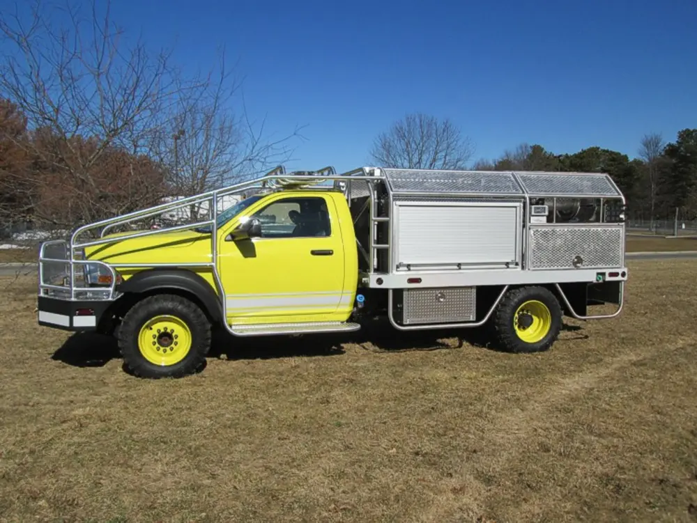 Exterior view of small fire truck showing cab, body compartments, and wheel/tire area.