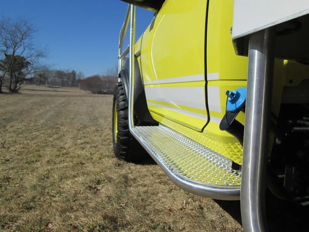 Exterior view of small fire truck showing cab, body compartments, and wheel/tire area.