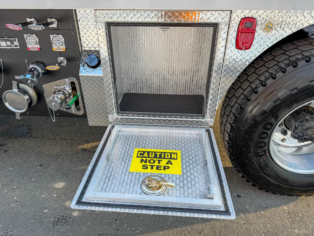 Lower side tank compartment open beside the pump panel and rear wheel.