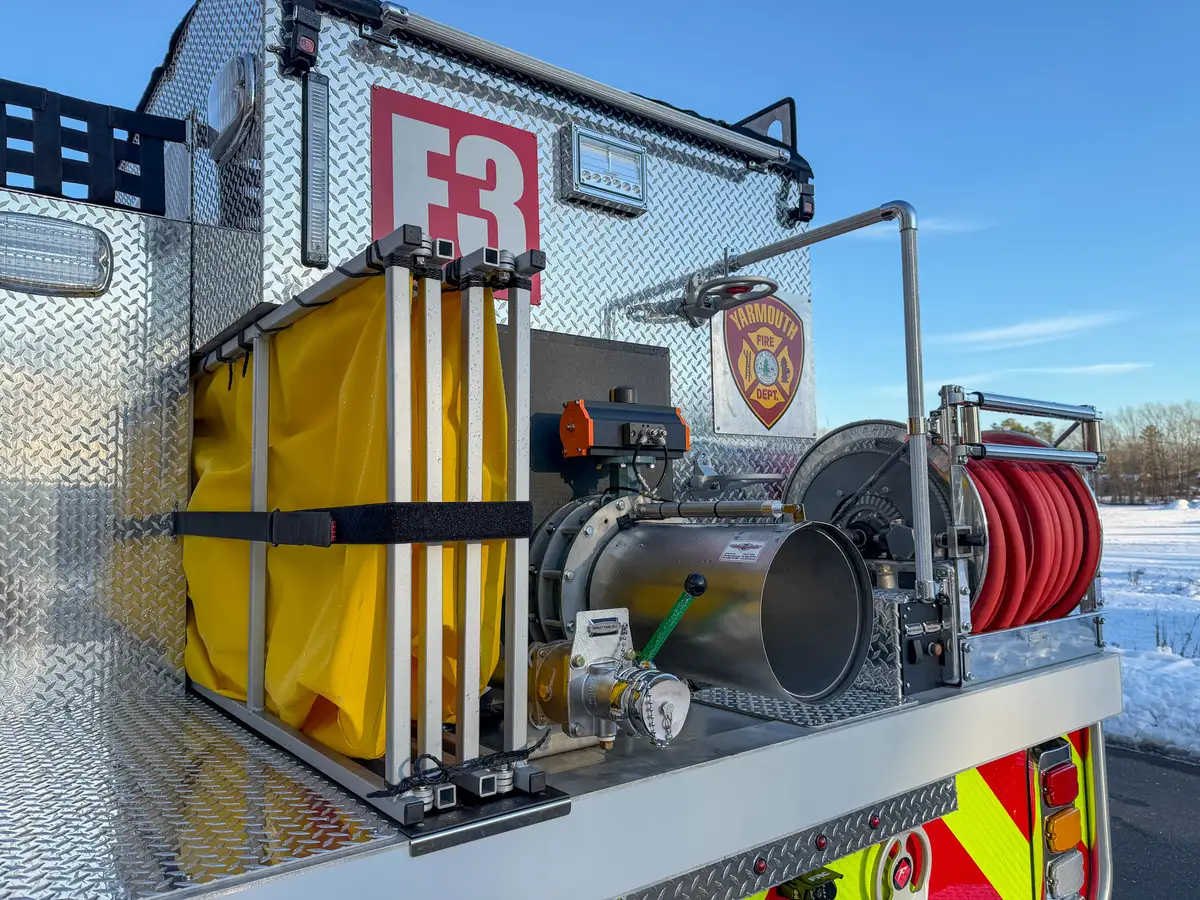 Rear corner close-up of folded yellow dump tank and dump chute assembly.