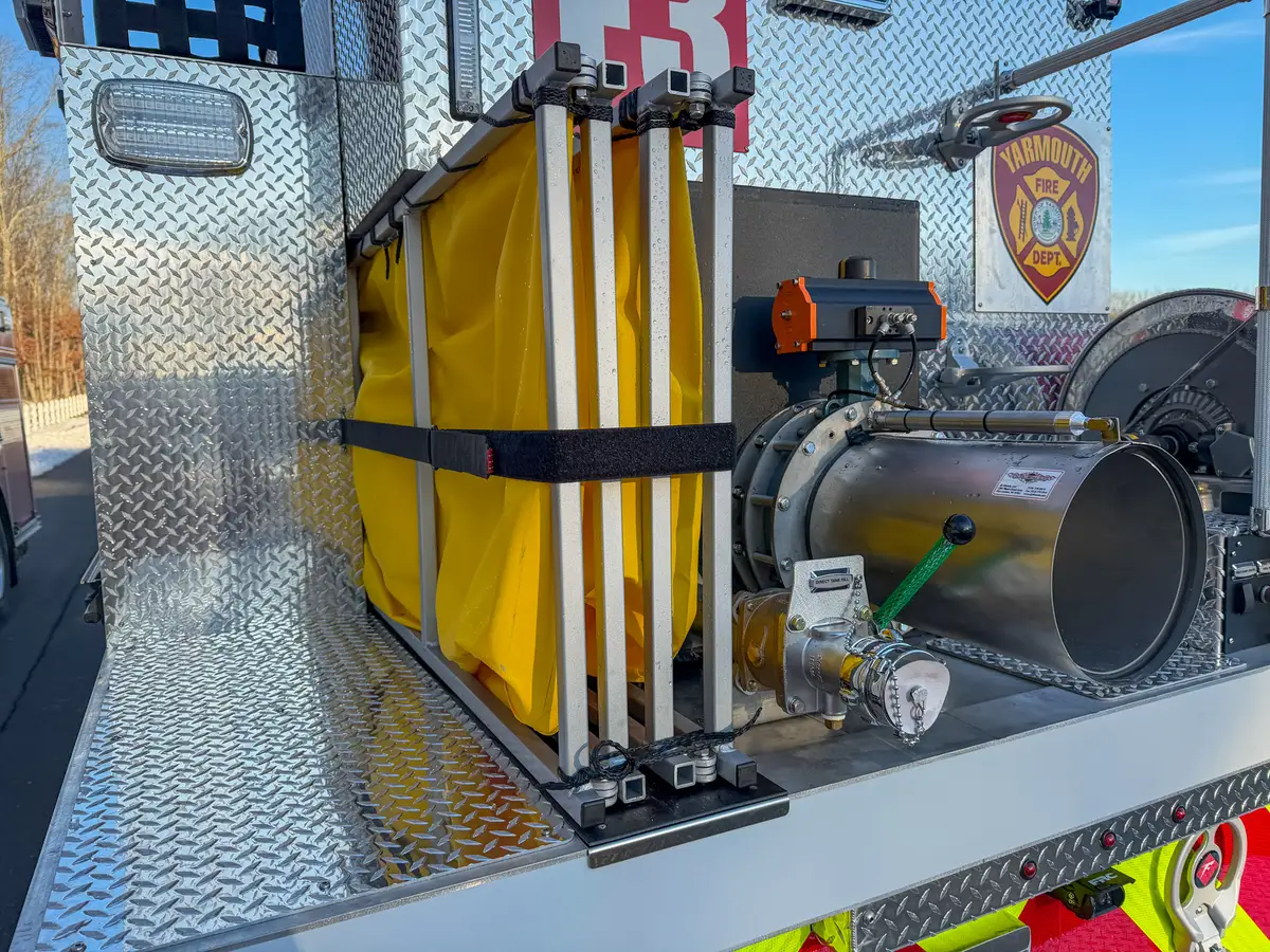 Close-up of folded dump tank frame and rear dump chute actuator hardware.