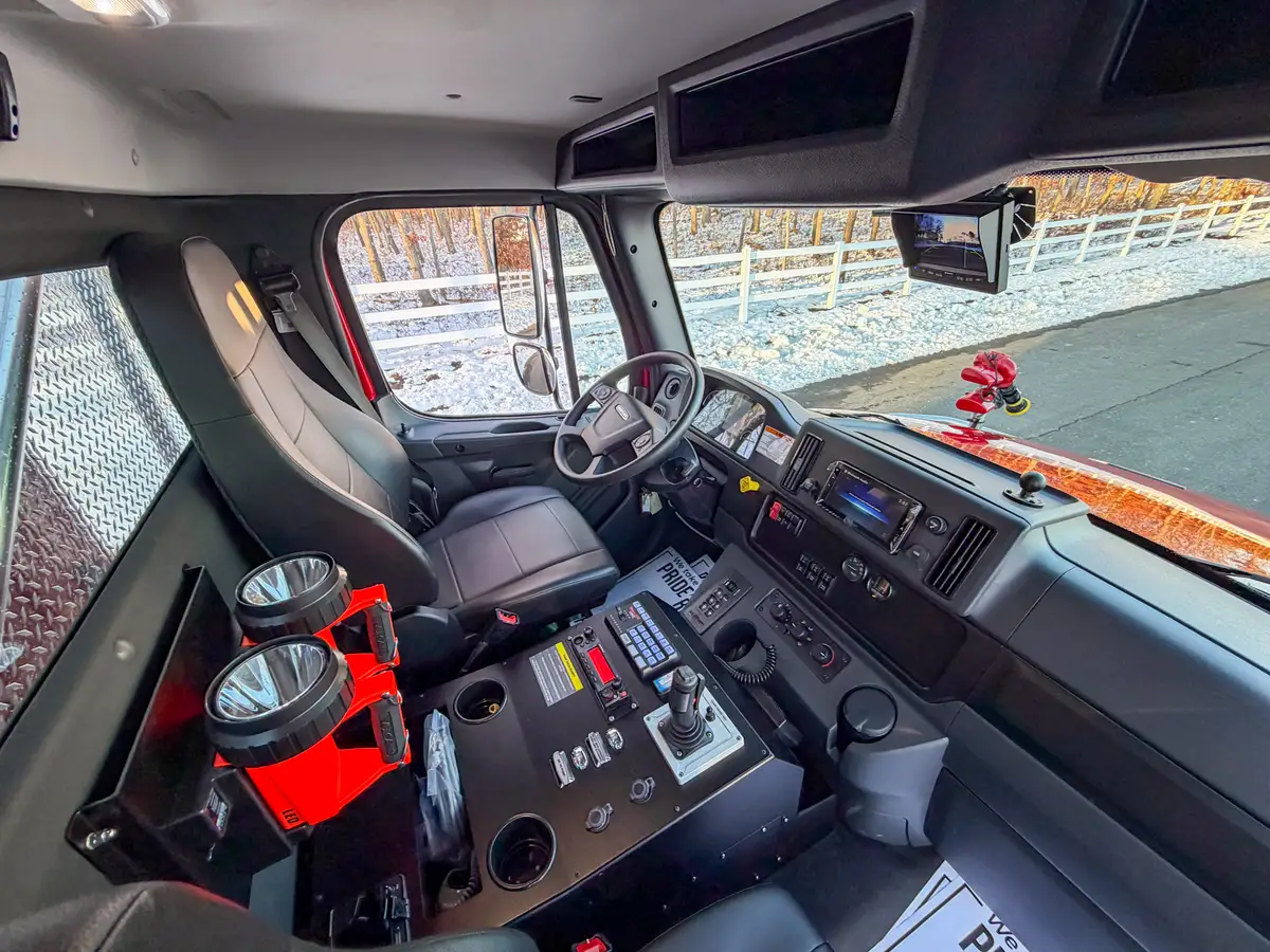 Interior side view with driver seat, steering wheel, and center console controls.