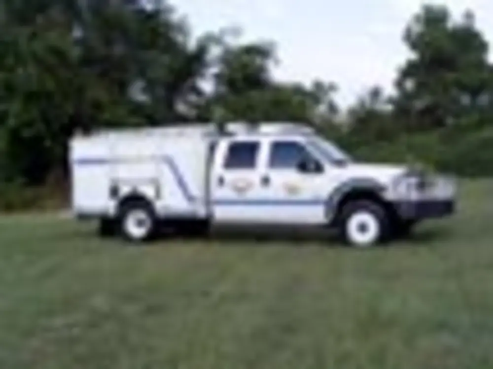 Exterior view of small fire truck showing cab, body compartments, and wheel/tire area.