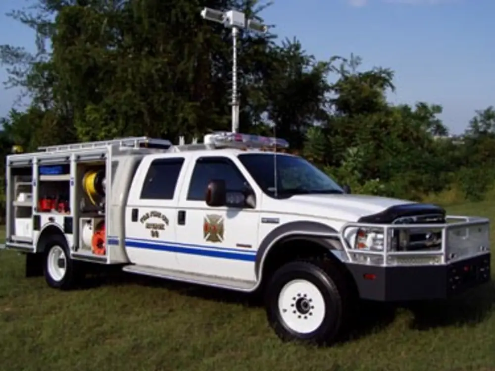 Exterior view of small fire truck showing cab, body compartments, and wheel/tire area.