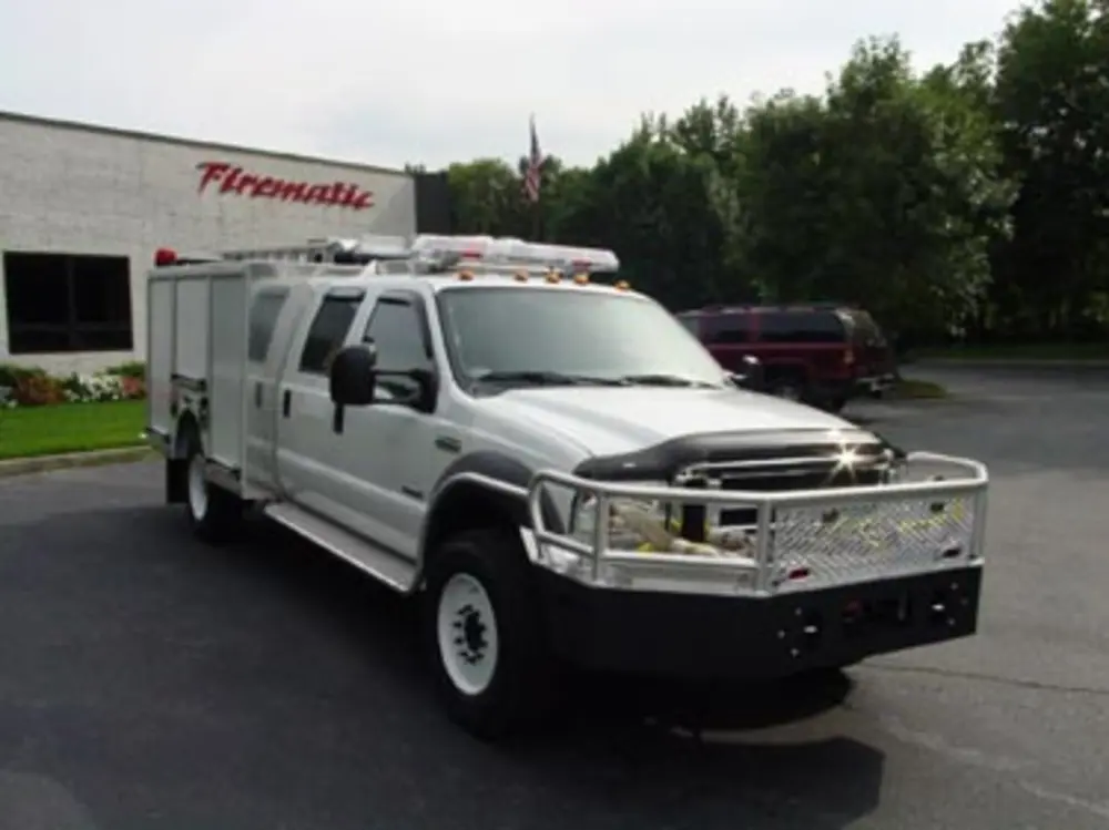 Exterior view of small fire truck showing cab, body compartments, and wheel/tire area.