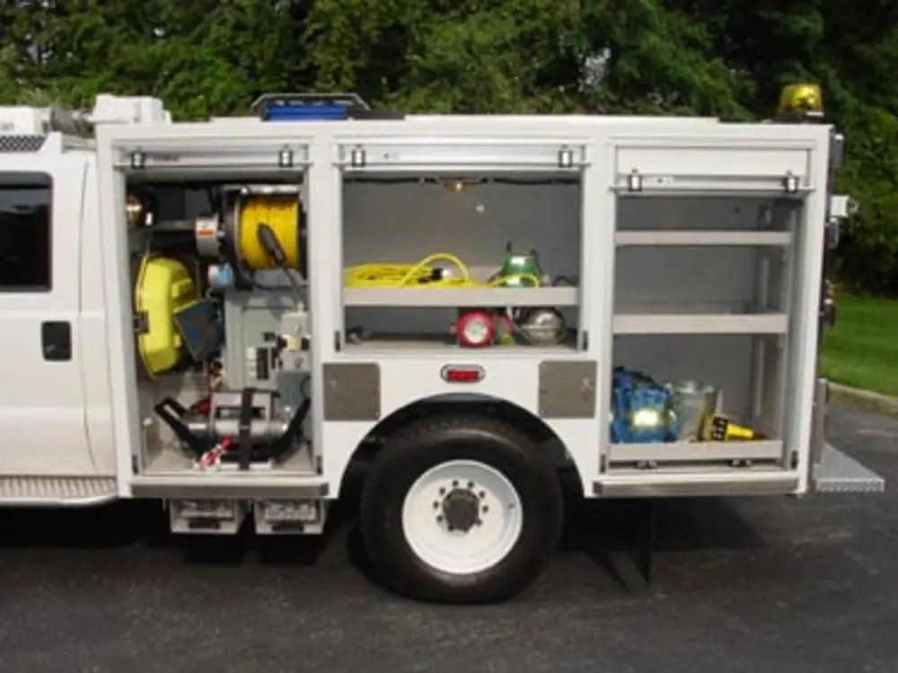 Exterior view of small fire truck showing cab, body compartments, and wheel/tire area.