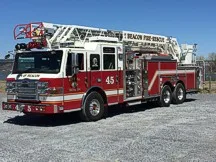 Wide front left view of the parked aerial ladder truck with bumper, cab, and ladder bed visible.