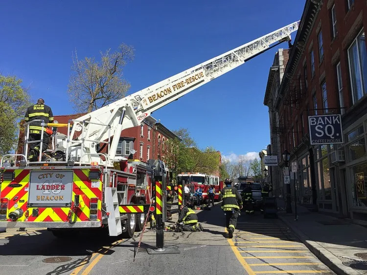 Rear street scene with the aerial ladder extended, rear stabilizers deployed, and firefighters working below.