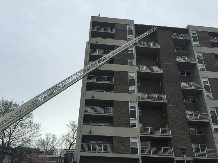 Extended aerial ladder reaching to an upper balcony level on a multi-story apartment building.