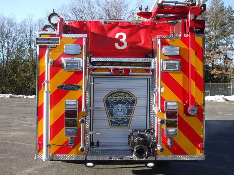 Straight rear view with red-yellow chevrons, rear roll-up door, and rear discharge connection.