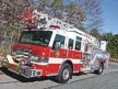 Wide front-right view of the ladder truck parked roadside with the aerial ladder bed visible.