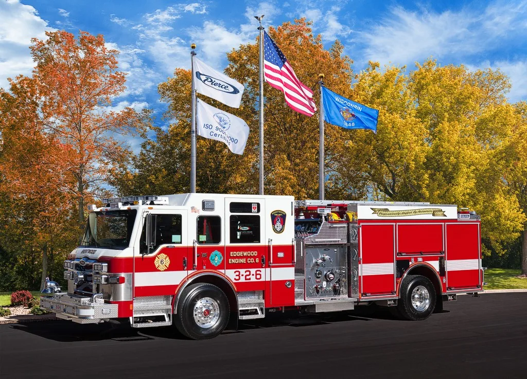 Driver-side profile of a pumper parked beneath flagpoles showing full side body and wheelbase.