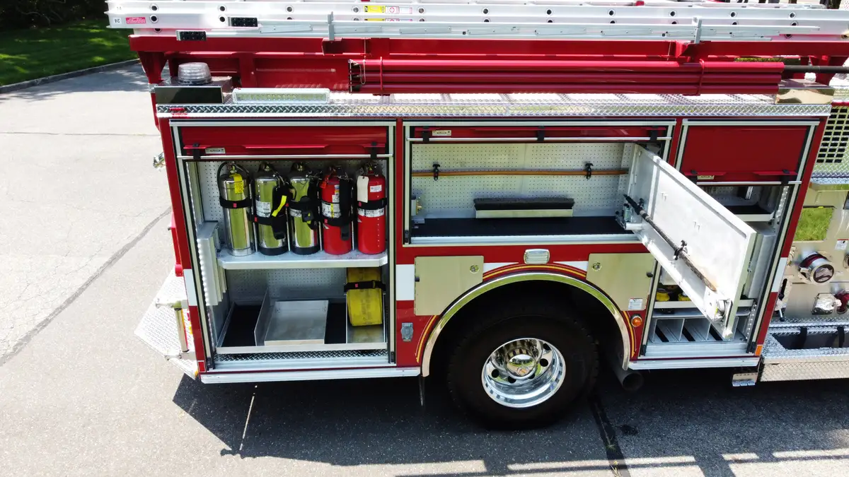 Pierce pumper aerial side view with open compartment showing extinguishers and mounted tools