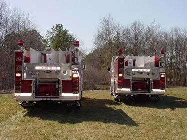 Rear view of two pumpers showing rear panels, warning lights, and hosebed openings
