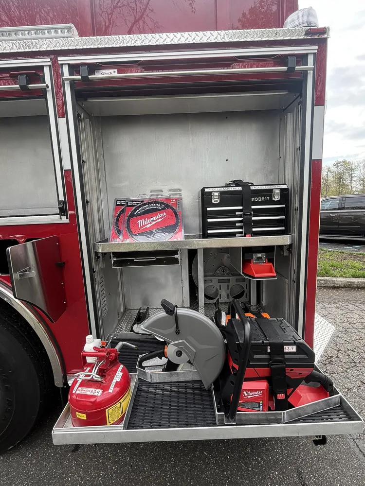 Open side compartment showing saw blades, tool chest, cutoff saw, and fuel can on pull-out tray