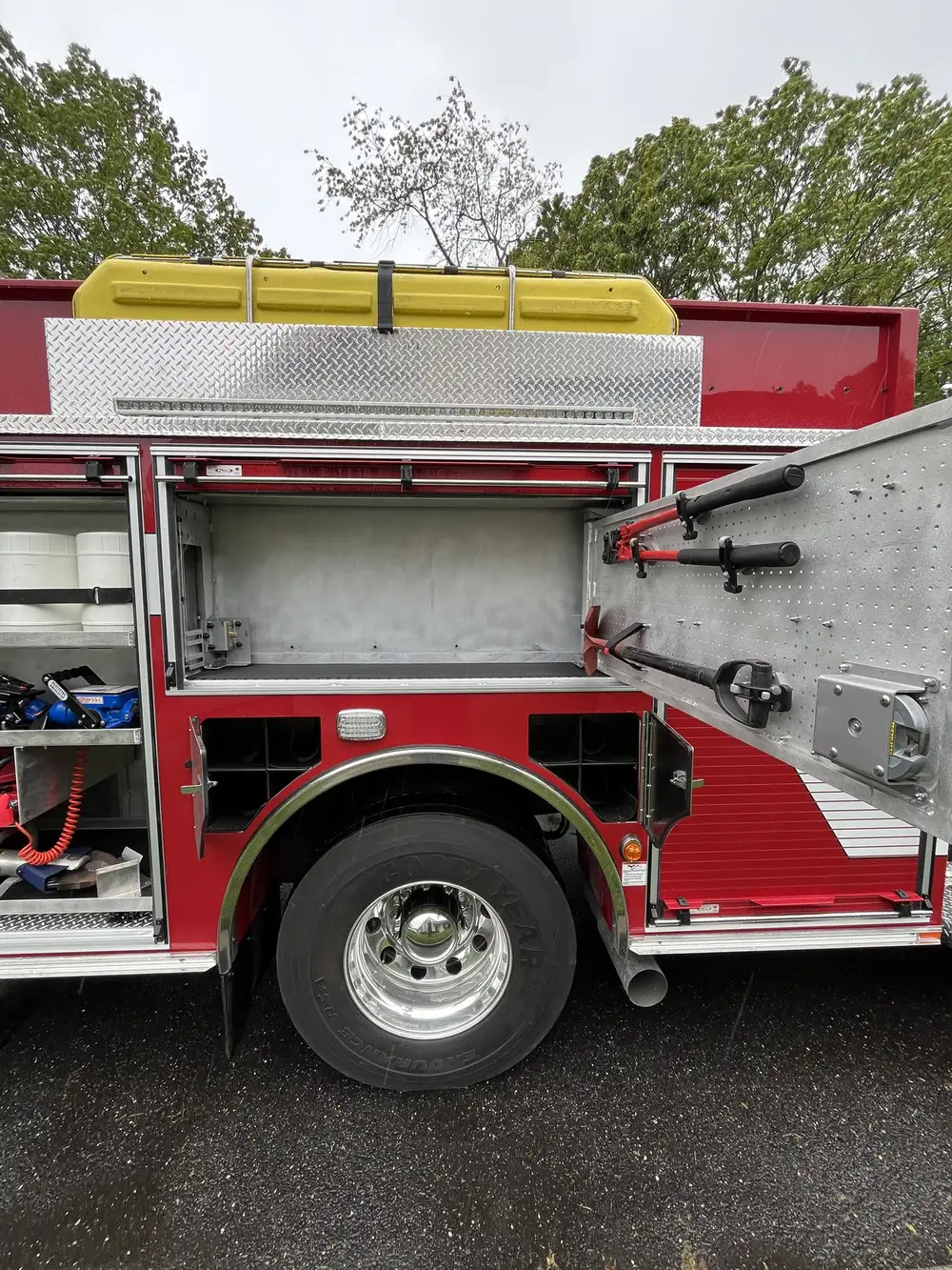 Open upper compartment above rear wheel with door-mounted tools and empty storage bay