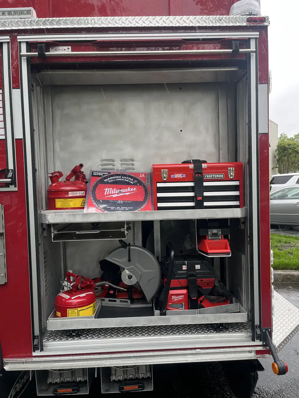 Open rear-side compartment showing saw, toolbox, fire extinguishers, and battery tools