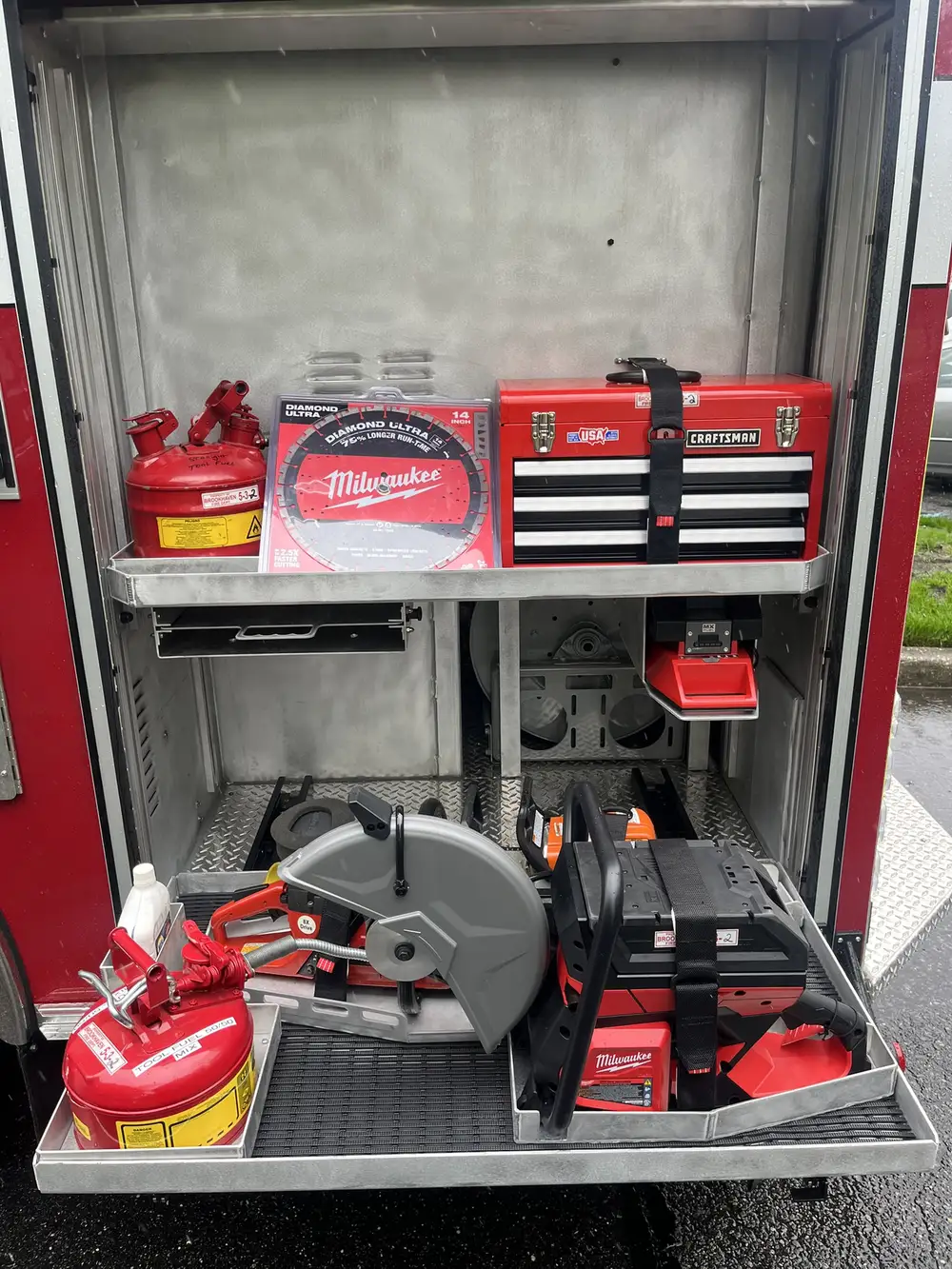 Open compartment with pull-out tray showing cutoff saw, battery tools, and extinguisher