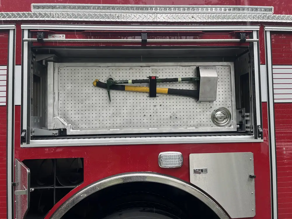 Open upper compartment above rear wheel showing mounted sledgehammer and hand tool brackets