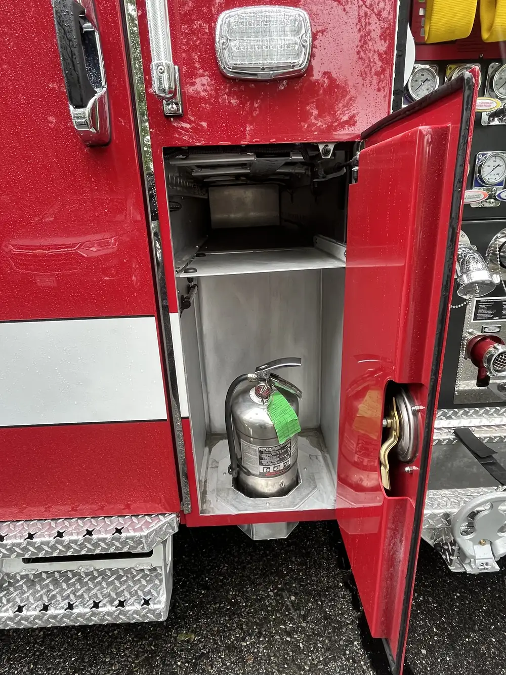 Narrow side compartment near pump panel showing mounted fire extinguisher and upper shelf