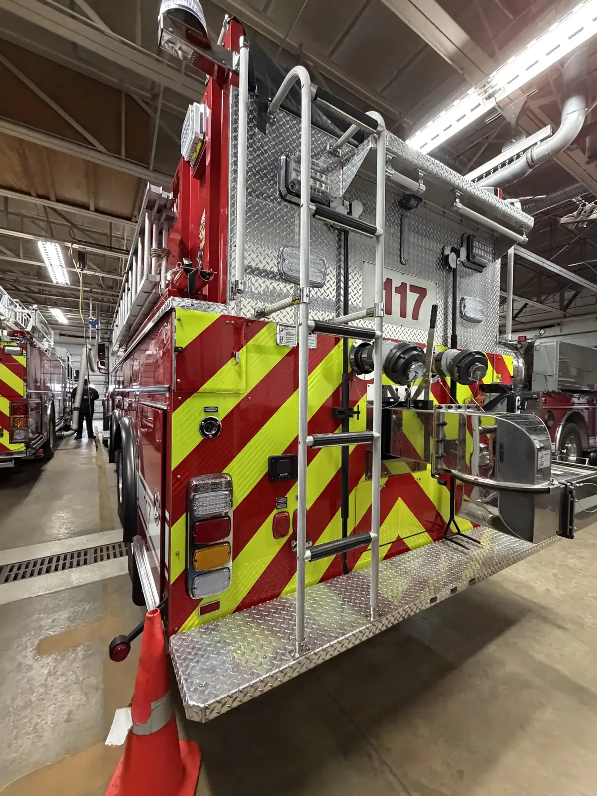 Rear-left view showing chevron striping, rear ladder, and rear dump assembly