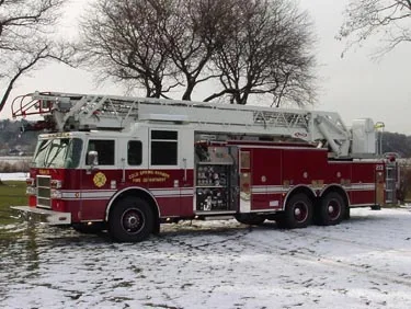 Driver-side profile view showing tandem rear axles, pump panel area, and ladder bed