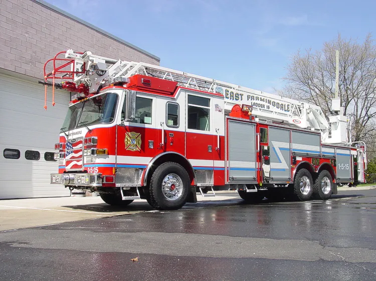 Front-left wide view showing the cab, bumper, side compartments, and aerial ladder bed.