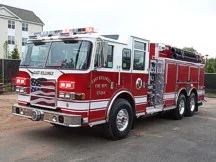 Wide front left angle of the parked apparatus with cab, bumper, and side body compartments.