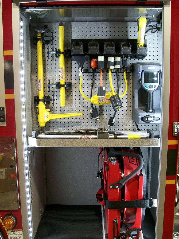 Open compartment showing hand tools, hydraulic components, and storage shelf