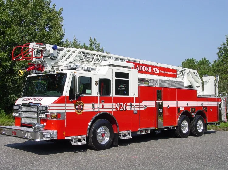 Front-right close exterior view highlighting the grille, ladder bed, side compartments, and tandem rear wheels.