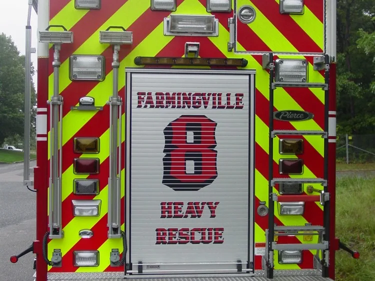 Straight rear close-up with red-yellow chevrons, rear roll-up door, scene lights, and access ladder.