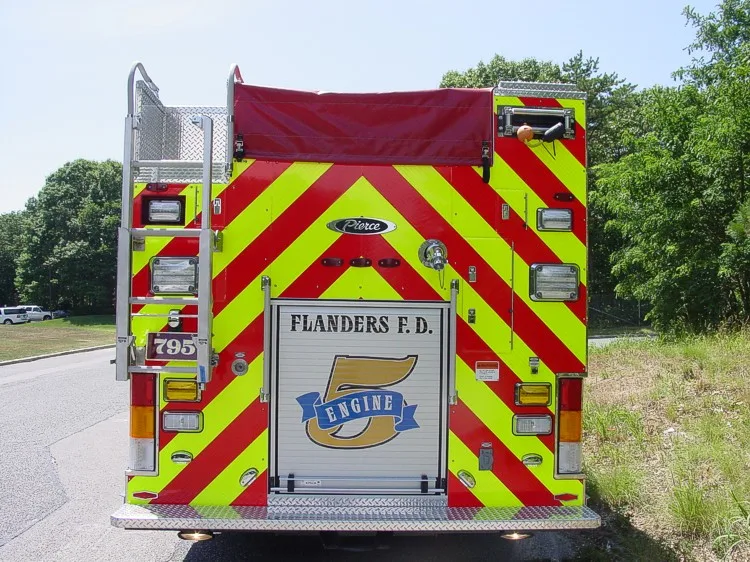 Straight rear view with red-yellow chevrons, rear roll-up door, warning lights, and ladder.