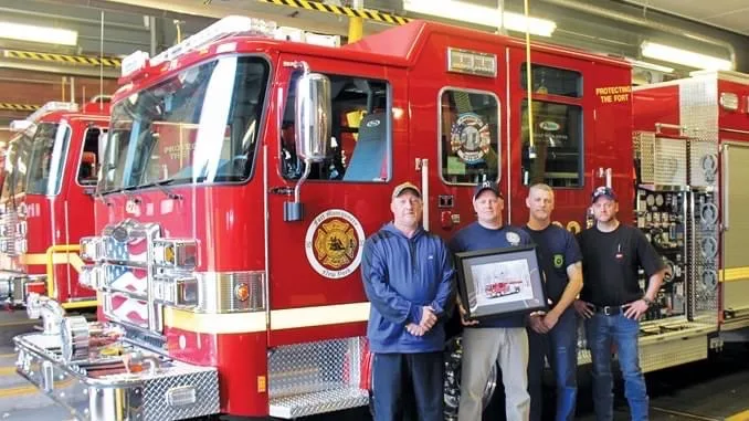 Crew photo beside pumper near front-right corner with open compartments
