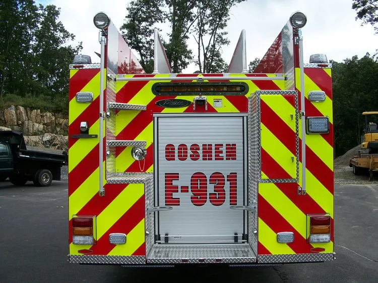 Straight rear view with red-yellow chevrons, rear ladder, warning lights, and center rear roll-up door.