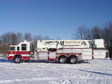 Driver-side full profile showing tower ladder body, side compartments, and tandem wheels