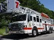 Wide front-left view of the ladder truck parked roadside with full aerial and side body visible.