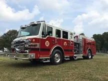Wide front-left view of the pumper parked on grass with cab, pump panel area, and side compartments visible.