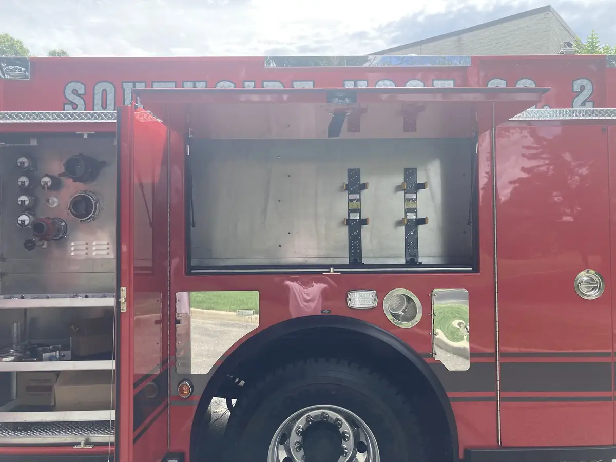Open tool compartment with mounted axes, cutters, saw, and extinguisher