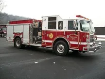 Wide left-front view of the parked apparatus showing bumper, cab, and body compartments.