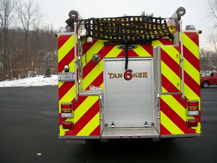 Straight rear view with red-yellow chevrons, rear roll-up door, and hosebed cover netting above.