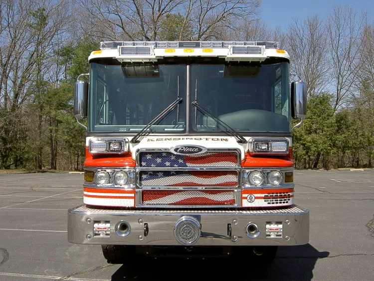Head-on front view showing the chrome bumper, flag-style grille, windshield, and roof warning lights.