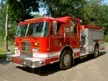 Wide front right view of the parked pumper with chrome bumper, cab, and body compartments.