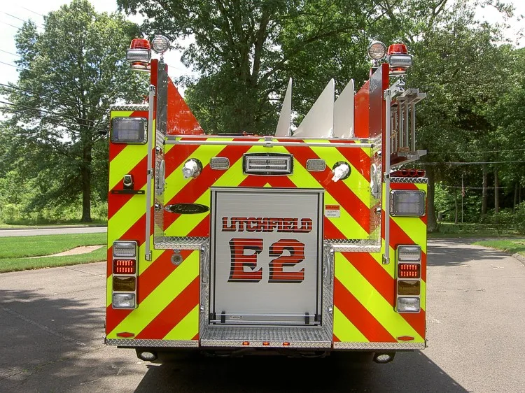 Straight rear view with red-yellow chevrons, rear roll-up door, scene lights, and corner warning lights.