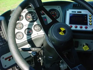 Driver cockpit close-up showing steering wheel, gauges, and dashboard controls