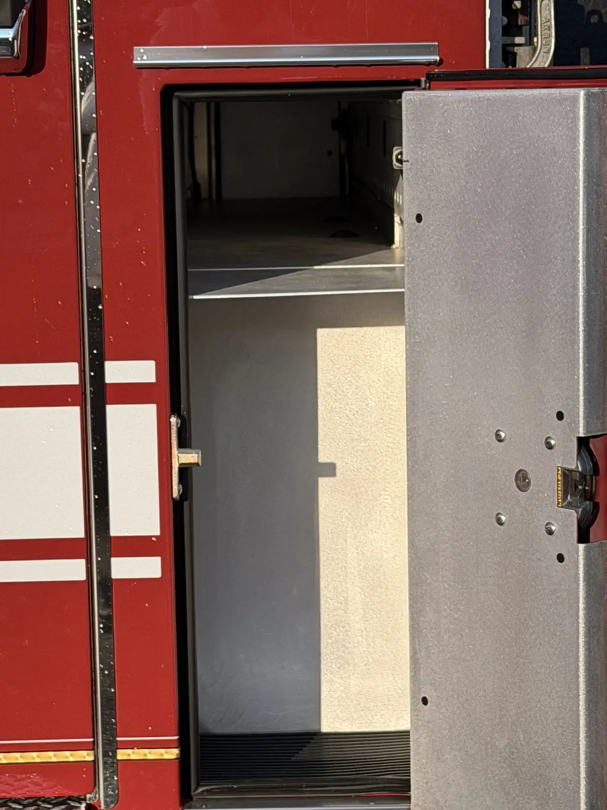 Narrow side compartment open behind cab showing tall empty storage bay