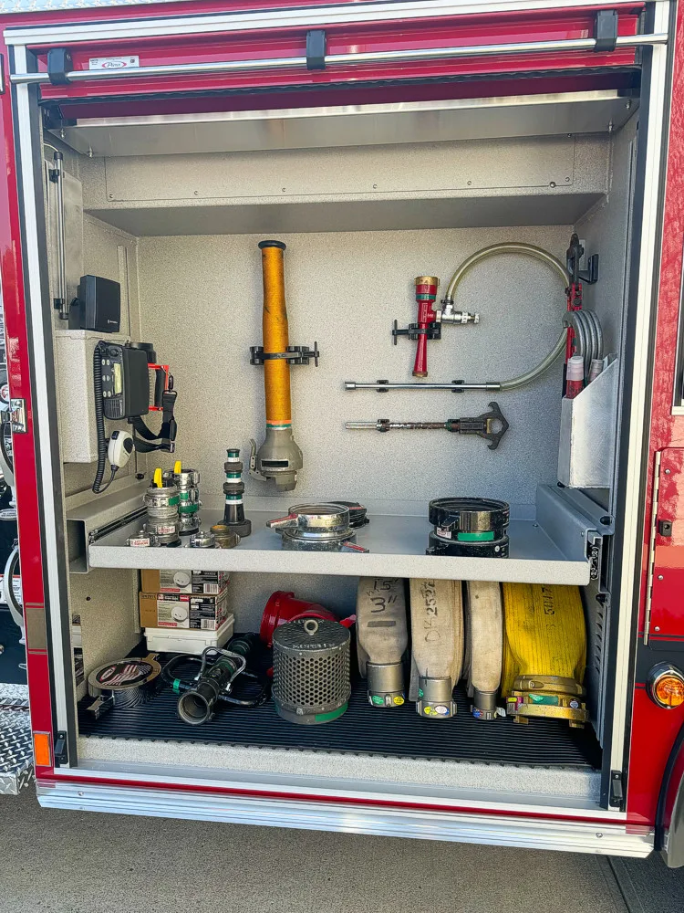 Open side compartment showing stored hose adapters, nozzles, hand tools, and portable equipment.