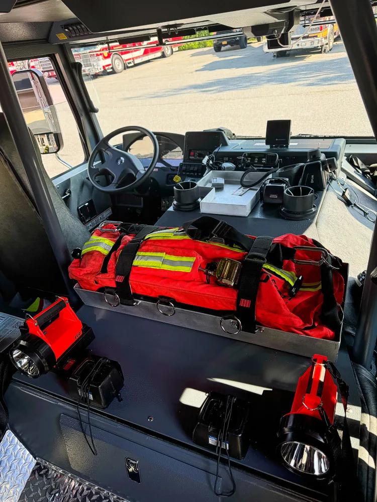 Cab interior view toward the driver area showing steering wheel, dashboard controls, console electronics, and seats.